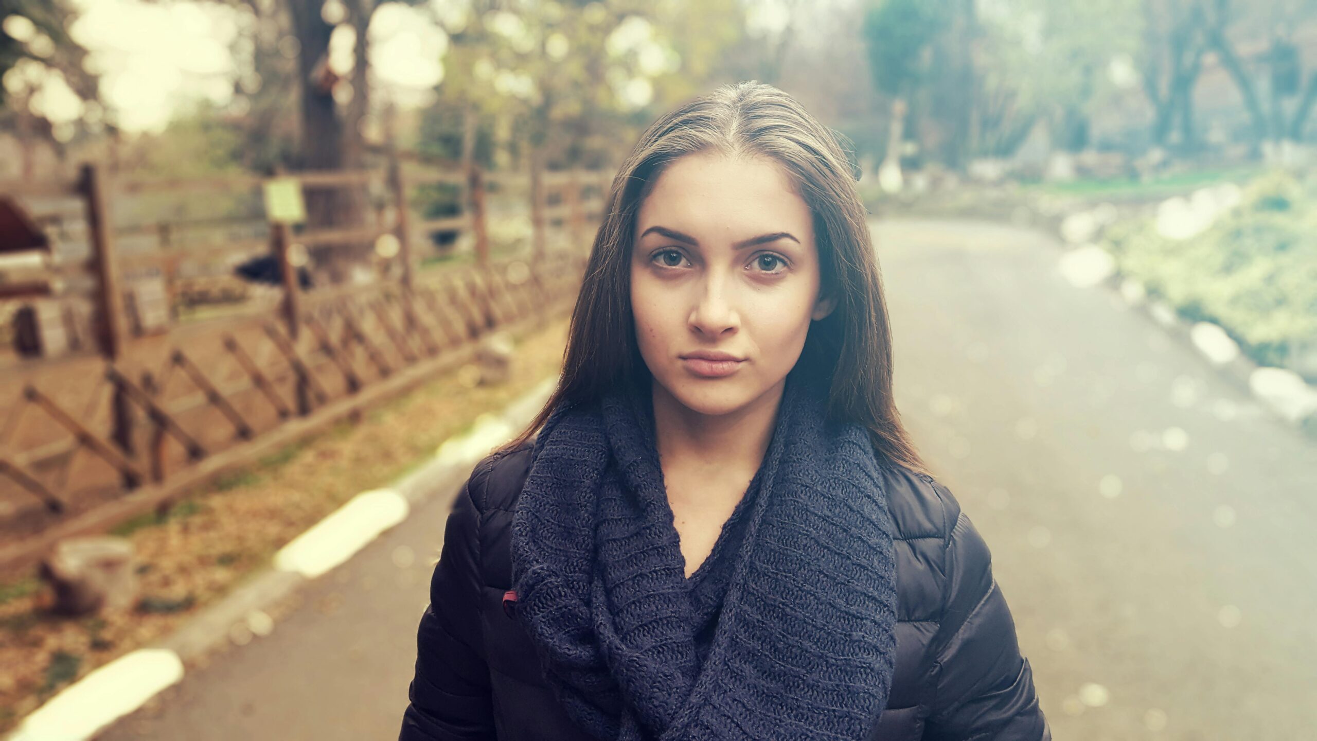 Young woman in a cozy scarf poses confidently in an autumn park.